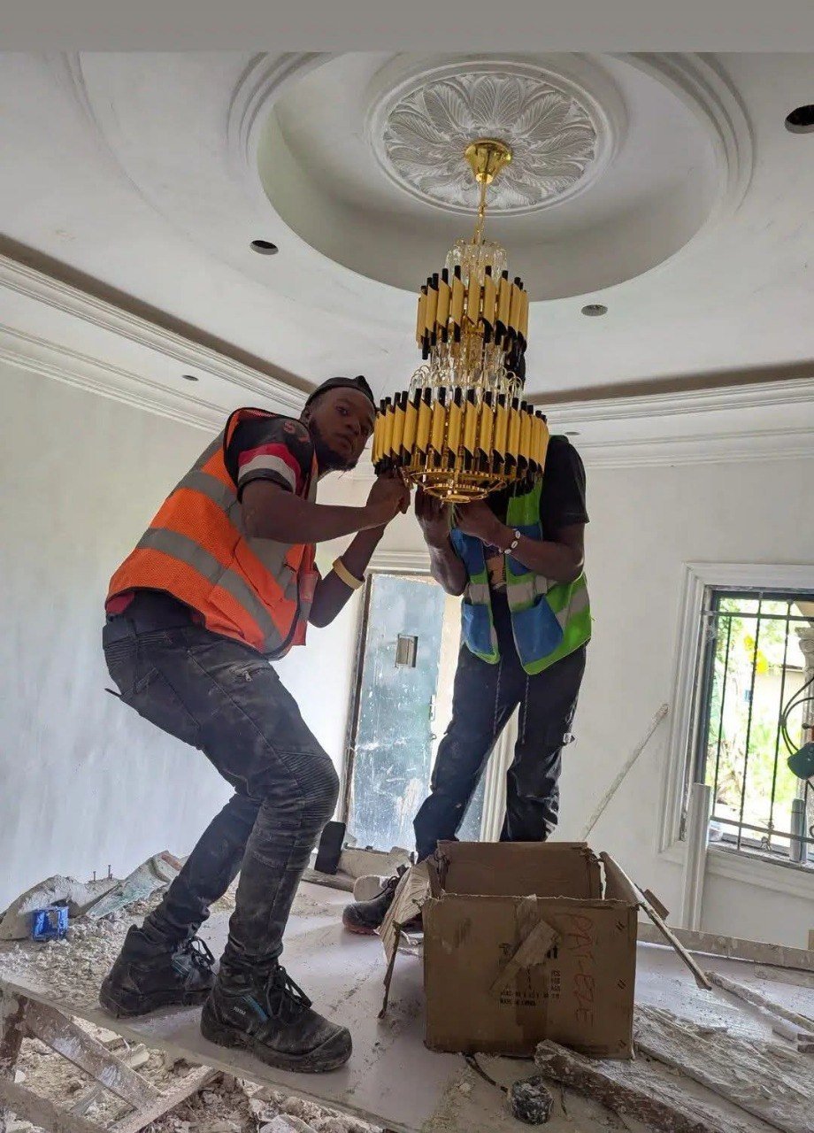 Deux techniciens installant un lustre en cristal au plafond
