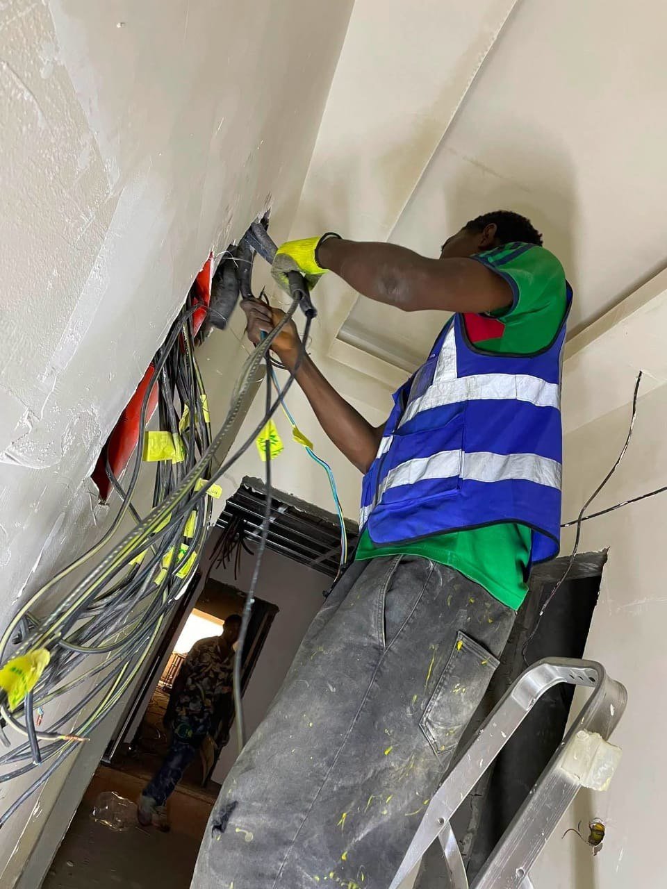 Technicien tirant des câbles électriques en plafond depuis une échelle