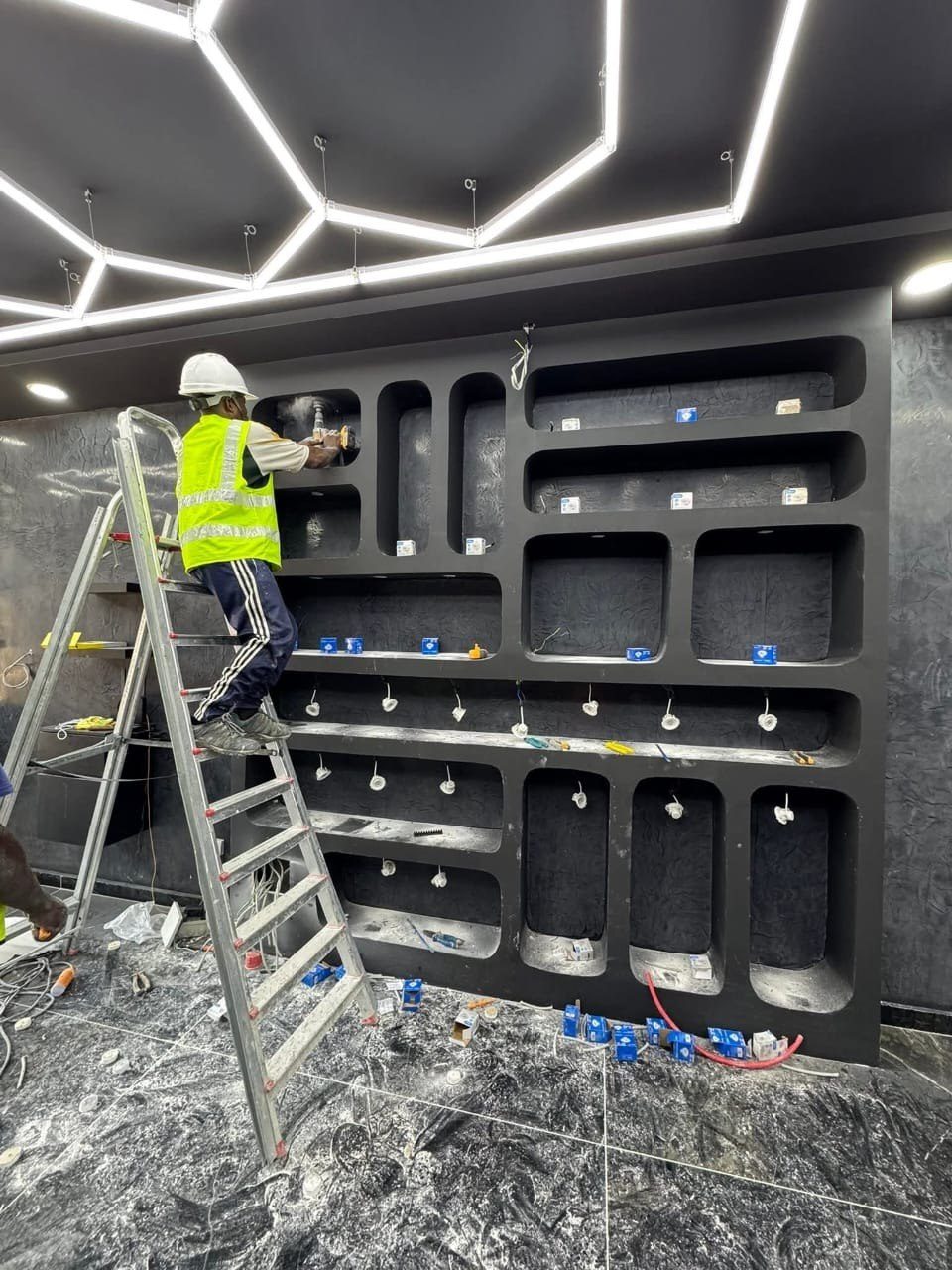 Technicien installant l'éclairage encastré de niches menuisées sous un plafond hexagonal LED